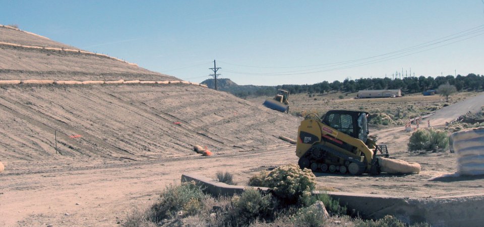 Construction vehicles working on a dusty hillside.