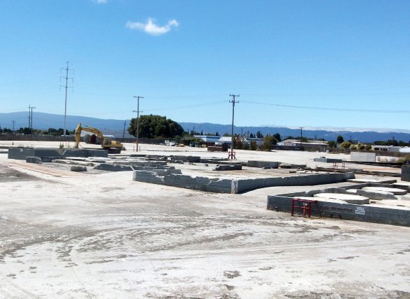 Empty industrial lot with concrete building foundations and construction equipment visible