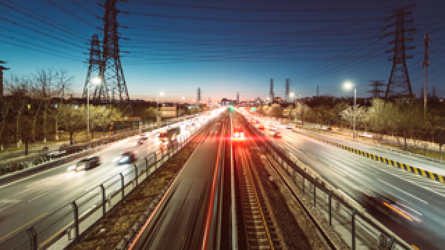 Photo: Highway vehicles and trains in motion at night.