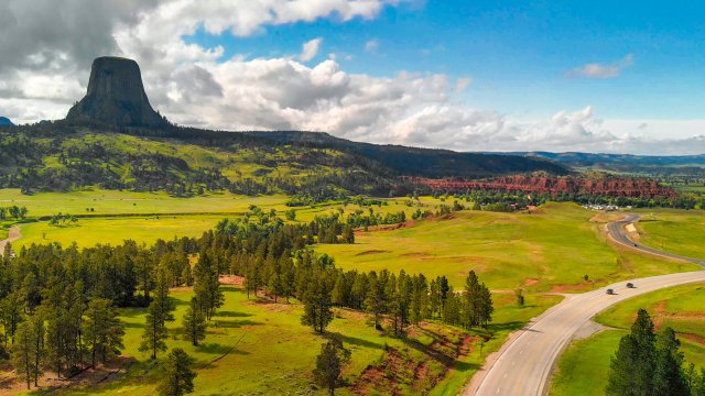 aerial view of a road winding through green fields with Devil's Tower seen in the distance off to the left. Adobt Stock file.