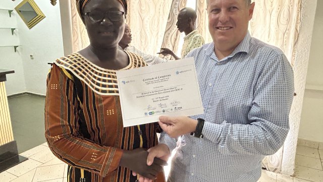 Woman in brown dress smiling at camera while receiving a certificate of completion next to a smiling man wearing sky blue dress shirt.