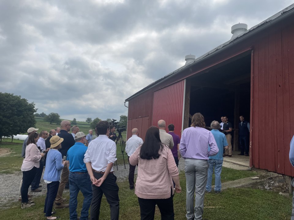 Officials are seen behind a podium talking to a group on a farm