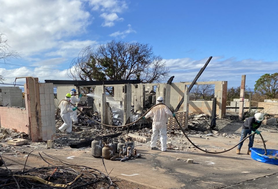 Crews applying the soil stabilizer to the ash and debris footprint of a burned building.