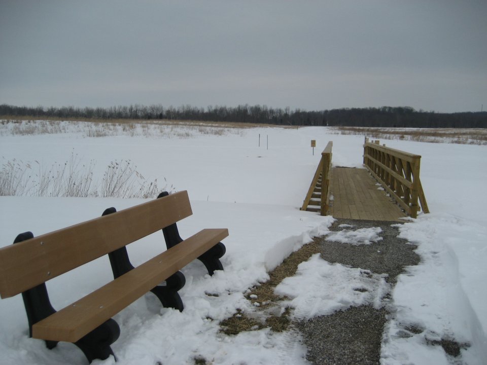 A bench and small pedestrian bridge in a snowy area.