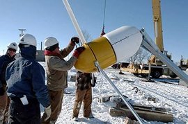 Several people looking at a piece of equipment, and snow on the ground.