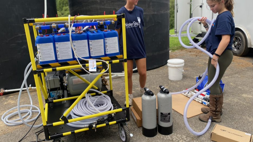 Two people setting up a WOW Cart, a yellow framed card with jugs, tubes, and other equipment.