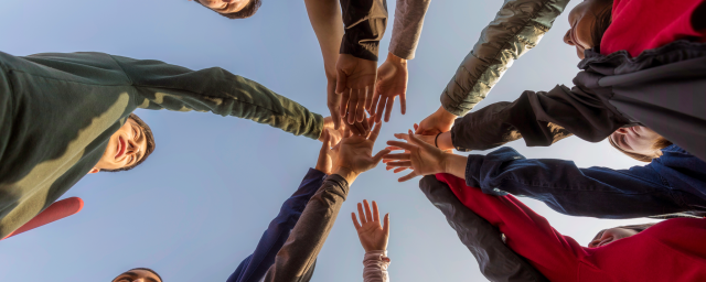 A group of people put their hands together in the middle of a circle, indicating teamwork