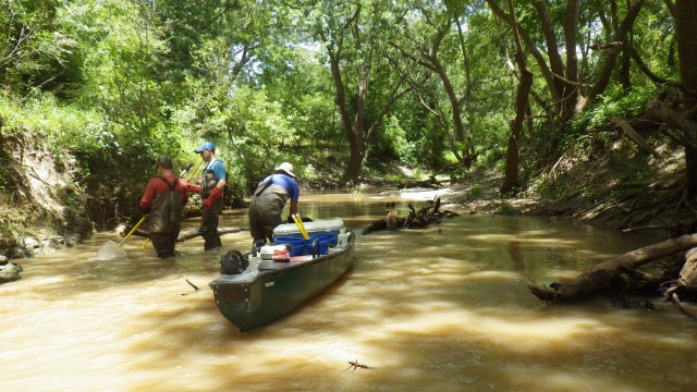 Crew in turbid stream with boat full of equipment