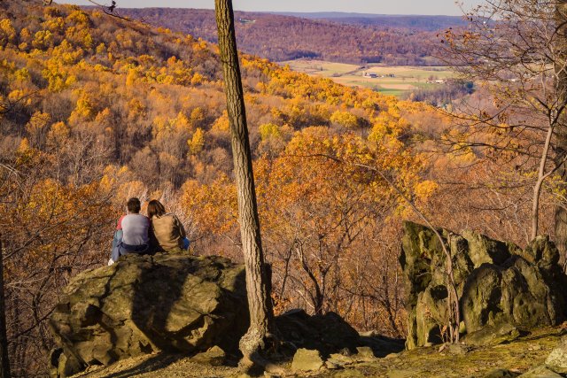 People sitting together on a large boulder on a hillside overlooking a valley.