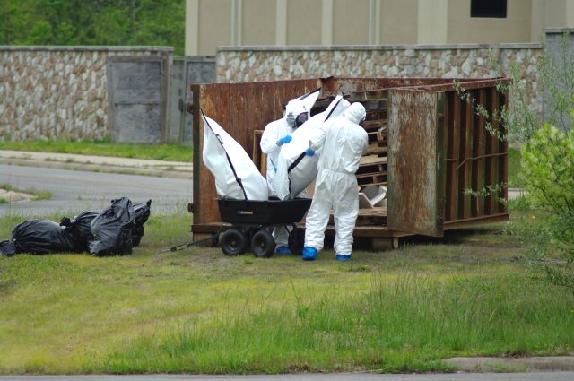 Two team members in tyvek suits placing waste bags into a roll-off container.