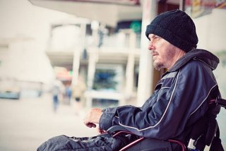 Man seated in a wheelchair on the sidewalk.