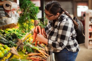 A young woman inspects produce in a grocery store display.