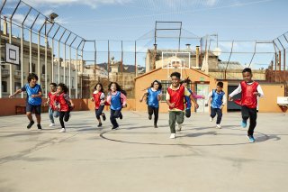 A group of young children in red and blue jerseys run across a playground.