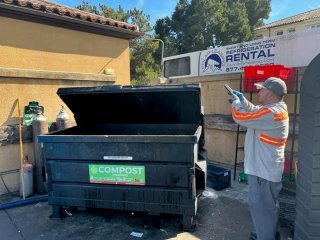 A person holding a mobile phone scanning a large compost waste bin.