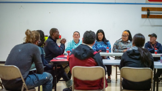 A group of people are sitting in folding chairs around a table.