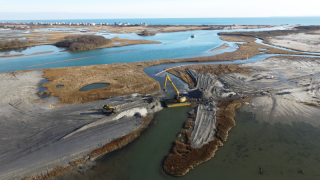 An aerial view of a crane sitting on a dredge boat and moving sediment.