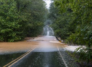 An image of a road with water flowing across it and blocking passage.