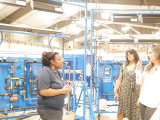 The image shows several people in a factory-setting at a community college in Gonzales, Louisiana.