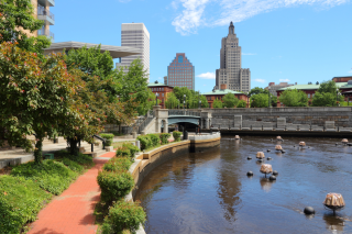 Water and trees in the foreground with city skyline in the background against a blue sky.