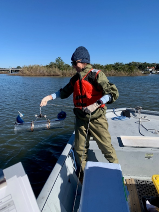 Dr. Jenny Paul in a wetsuit and lifejacket on a fishing boat holding a metal tube.