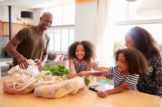 Family of four with two children unload vegetables from mesh reusable tote bags.