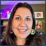 A person with long dark hair and beaded earrings.